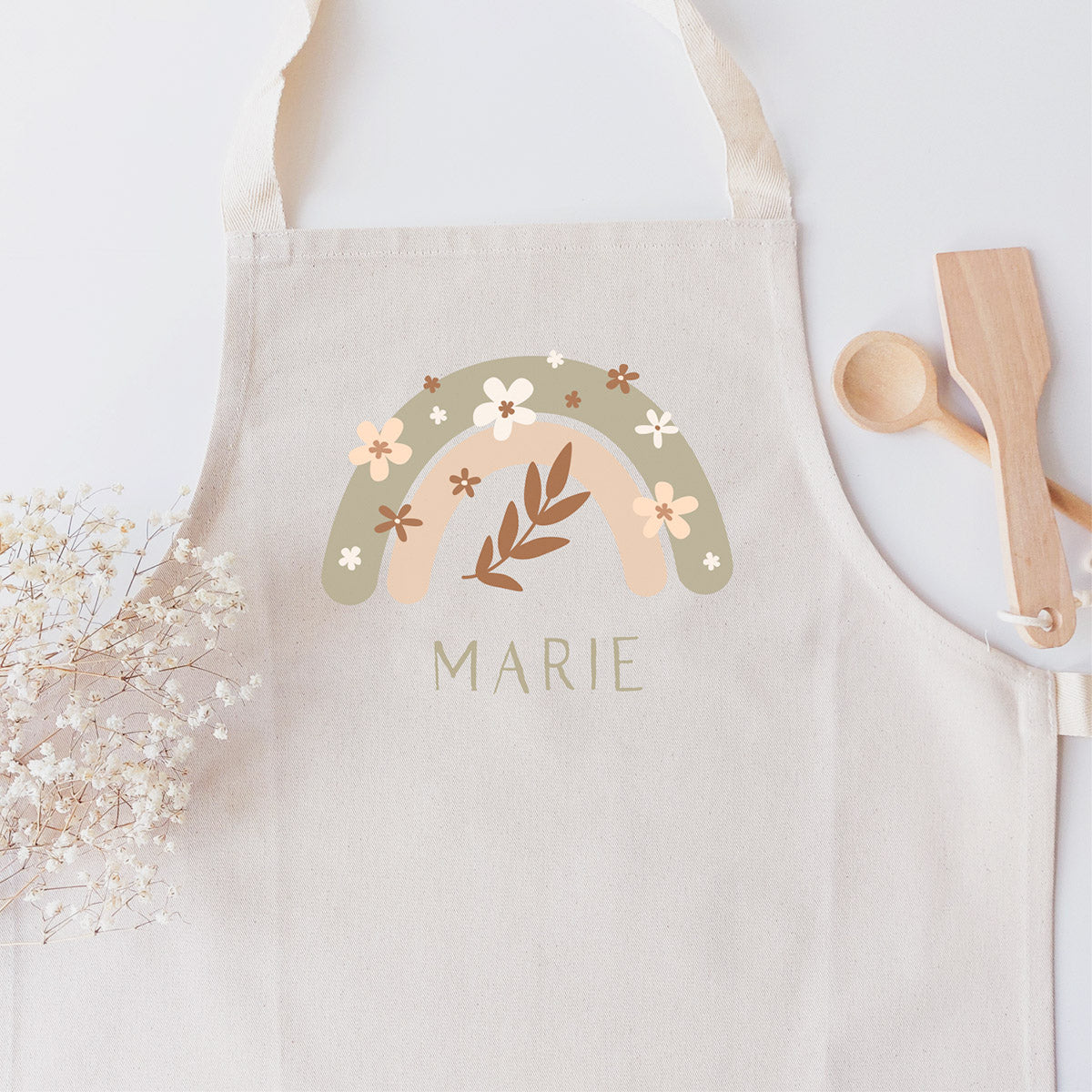 Kinderschürze mit floralem Boho-Regenbogen und personalisiert mit einem Namen mit pastellgrünen Großbuchstaben